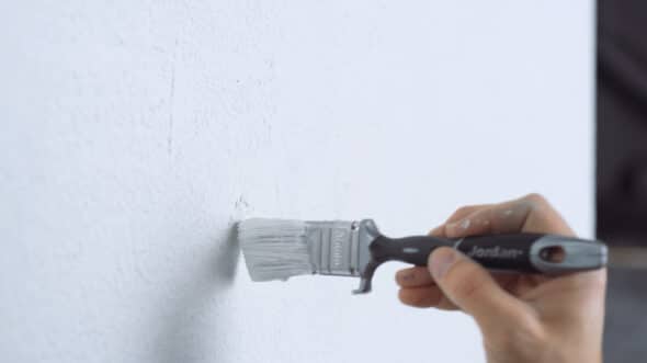 Person med liten malekost som maler en vegg